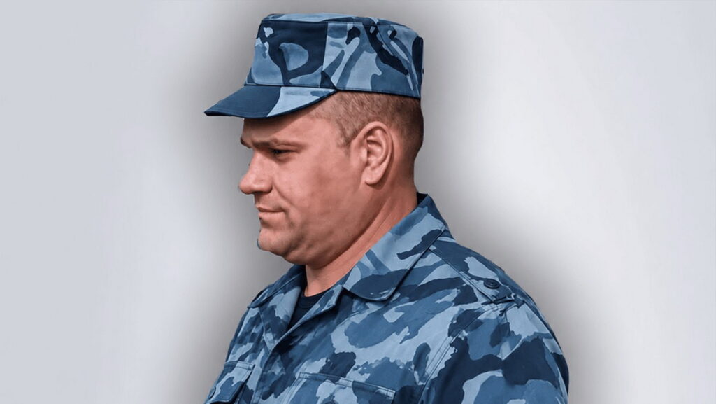 Чоловік у синій камуфляжній формі та кашкеті стоїть боком до камери